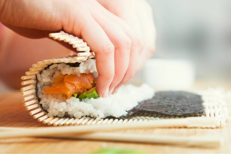 Mains en train de rouler un maki sushi avec un makisu